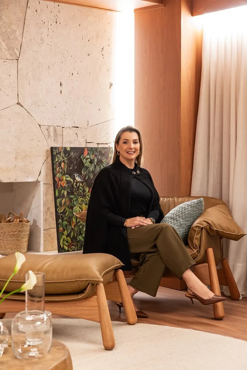 Gizelle sentada em uma poltrona, diante de uma parede de pedra